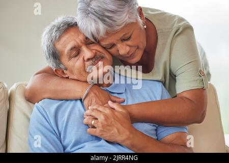 Abbraccio, conforto o sostegno di una coppia anziana triste o infelice in un soggiorno a casa. Marito anziano che soffre di problemi di depressione dopo il pensionamento Foto Stock