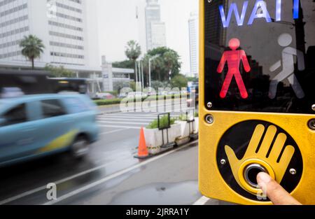 Persona toccare il pulsante del cartello pedonale situato in una strada trafficata della città Foto Stock