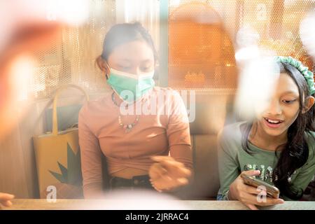 Due ragazze adolescenti del sud-est asiatico ritrovano insieme in un ristorante con solo uno di loro che indossa la maschera Foto Stock