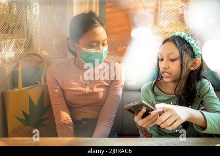 Due ragazze adolescenti del sud-est asiatico ritrovano insieme in un ristorante con solo uno di loro che indossa la maschera Foto Stock