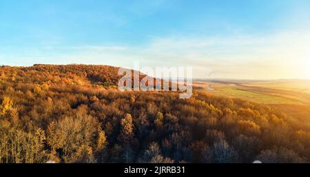 Vista aerea delle colline ricoperte di pini scuri e foreste rigogliose con baldane verdi e gialle nei boschi di montagna autunnali al tramonto. Bellissimo Foto Stock