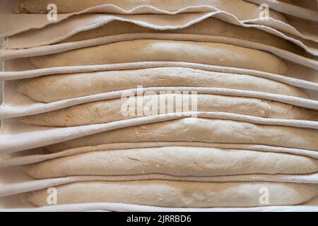 Il processo di fabbricazione di baguette francesi tradizionali in un panificio artigianale. Pane di prova su tessuto. Vista frontale. Foto Stock