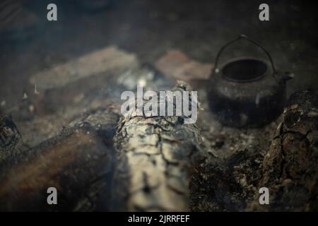 Bollitore acceso al fuoco. Cottura del tè su carboni. Dettagli del campeggio. Pentole in acciaio. Foto Stock