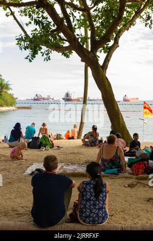 Rilassatevi sulla spiaggia di Siloso con navi portacontainer ancorate al largo, sull'Isola di Sentosa, Singapore Foto Stock