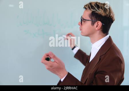 Un professore universitario che disegna nel mezzo di una classe sulla lavagna. Elegante uomo in tuta che dà una scrittura di classe nella lavagna bianca. Foto di alta qualità Foto Stock
