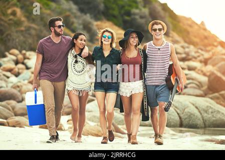 Pronti per una giornata in spiaggia. Foto a tutta lunghezza di un gruppo di amici che cammina sulla spiaggia in una giornata estiva. Foto Stock