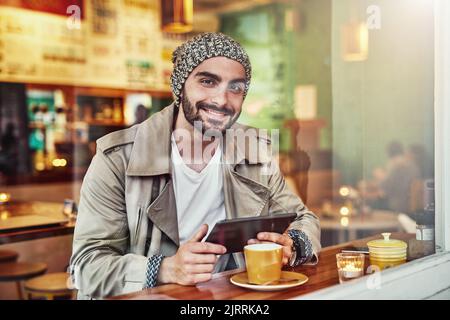 Venite per il wifi, restate per il caffè. Caldo di bel giovane uomo che utilizza un tablet digitale mentre si siede al bancone in un bar. Foto Stock