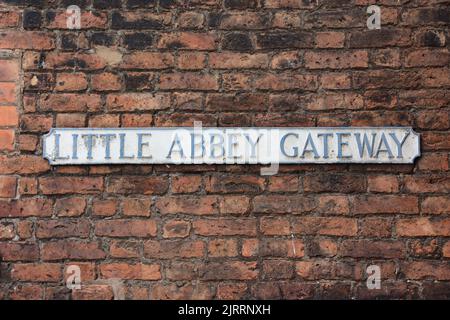 Un cartello con il nome di una strada sbiadita per Little Abbey Gateway montato su un muro di mattoni rossi Foto Stock