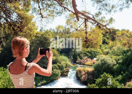 Bella ragazza adolescente che scatta foto della cascata. Krka cascate Parco Nazionale, Croazia. Foto Stock