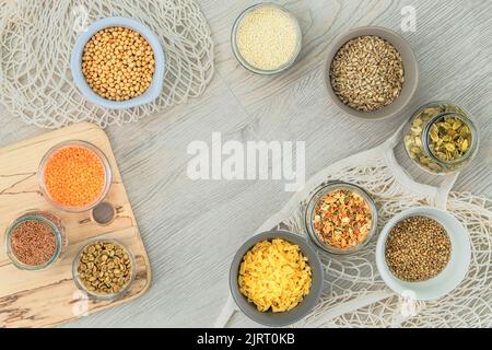 Set di prodotti biologici vegetariani in vasetti e ciotole di vetro su fondo di legno bianco. Vista dall'alto, spazio di copia. Foto Stock