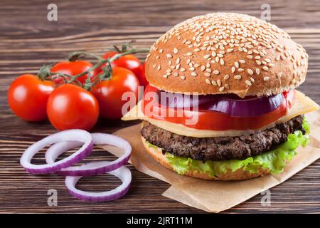 Cheeseburger fatto in casa con polpette di manzo, insalata fresca, pomodori e cipolla su conigli di condame, servito su un tavolo di legno marrone. Foto Stock