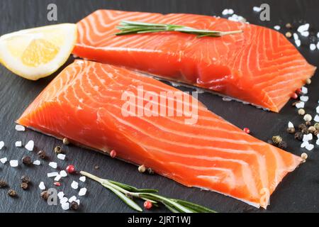 Due pezzi di filetto di salmone fresco con spezie su una superficie di ardesia nera Foto Stock