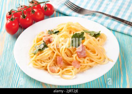 Pasta Carbonara con prosciutto e parmigiano servito su un piatto bianco su un tavolo di legno blu. Vista dall'alto, disposizione piatta Foto Stock