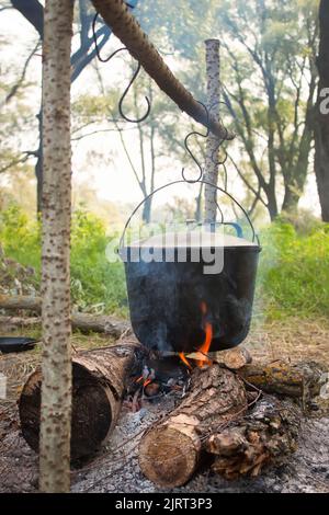 bollitore turistico affumicato sopra il fuoco del campo. Processo di cottura sulla natura. Foto Stock