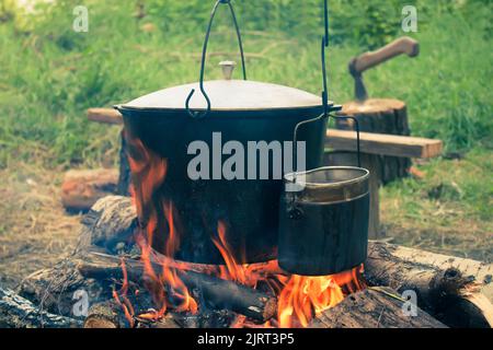 Due bollitori da turismo fumati sopra il fuoco del campo. Processo di cottura sulla natura. Vintage filtrato. Foto Stock