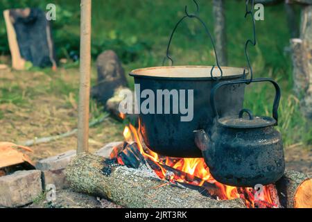 Due bollitori da turismo fumati sopra il fuoco del campo. Processo di cottura sulla natura. vintage filtrato Foto Stock