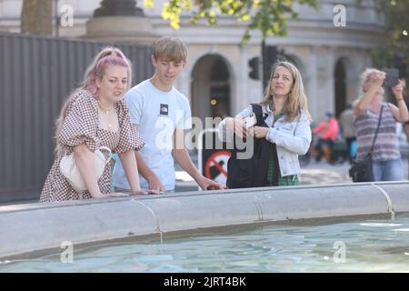 La gente gode delle fontane in Trafalgar Square, nel centro di Londra, mentre il tempo soleggiato segue una giornata di alluvioni e pioggia. Data immagine: Venerdì 26 agosto 2022. Foto Stock