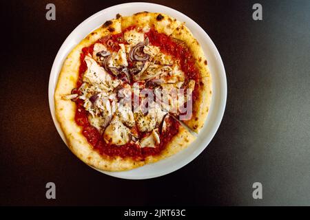 Vista dall'alto di una pizza con pollo e cipolle rosse su un piatto su un tavolo nero con copia spasper sul lato destro Foto Stock