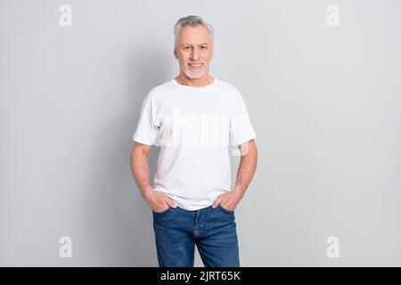 Ritratto di attraente uomo dai capelli grigi allegri che tiene le mani in tasche isolate su sfondo grigio color pastello Foto Stock