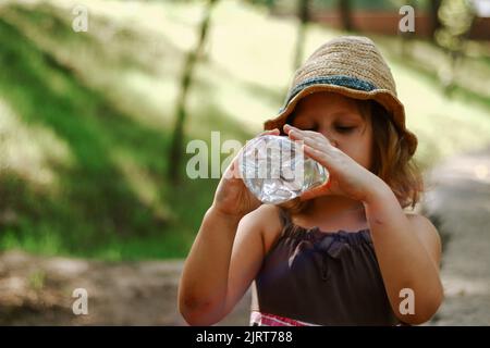 Il bambino beve acqua da una bottiglia di plastica. Bambino di 5 anni. Foto Stock