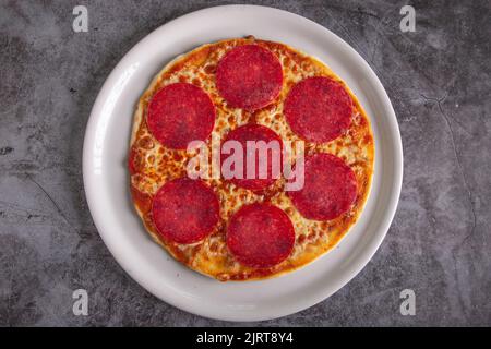 Gustosa pizza salame e ingredienti per la cottura, pomodoro su fondo di cemento nero. Hot salame pizza vista dall'alto. Piatto Lay Foto Stock