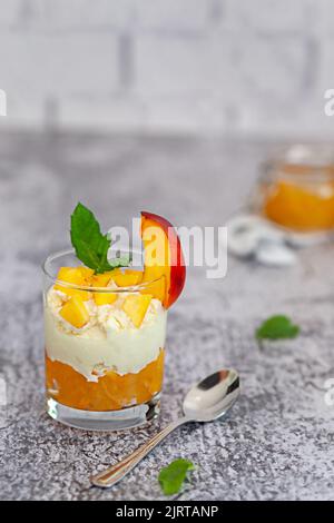 Dessert alla pesca in una tazza di vetro con crema cagliata e marmellata di pesche. Foto Stock