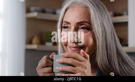 Sognante ispirato vecchia bionda grigio-capelli donna nonna nonna nonna maturo anziana pensionato donna di mezza età seduta in cucina bere caffè tè bevanda calda Foto Stock