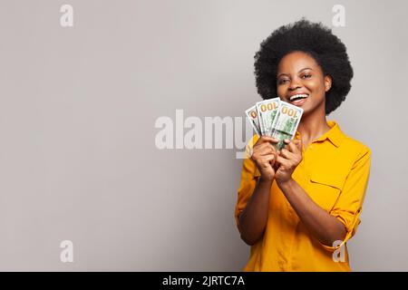 Felice giovane donna in possesso di centinaia di banconote in dollari e celebrare il successo su sfondo grigio. Finanza, moneta e concetto di persone Foto Stock