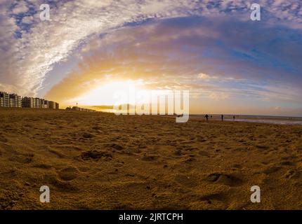 Tramonto autunnale a basso angolo sulla spiaggia di Koksijde con luce dorata e la gente che gioca sulla spiaggia Foto Stock