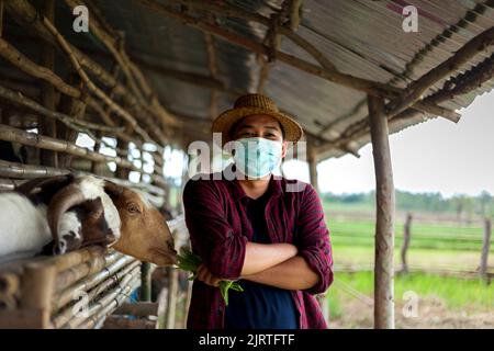 Un contadino tailandese fiero in piedi nella sua fattoria di capra con le braccia incrociate Foto Stock