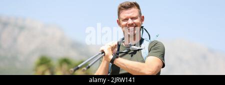 Giovane uomo sorridente in montagna con bastoni finlandesi Foto Stock