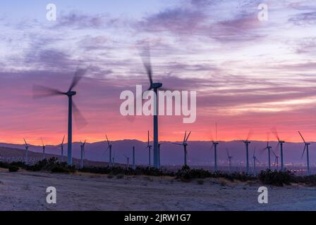 I mulini a vento che generano energia sulle montagne di Palm Springs, California, al tramonto girano mentre i venti forti passano. Foto Stock