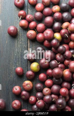 frutti di prugna sparsi del governatore su un piano da tavolo nero rustico, flacourtia indica, noto anche come ramontchi, susina malgascia o susina indiana Foto Stock