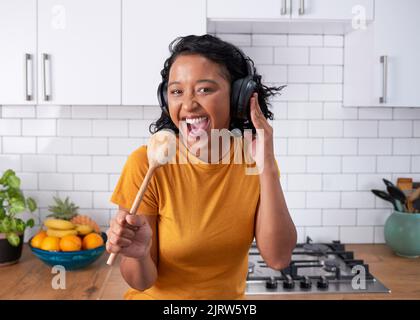 Una giovane donna funky canta con un cucchiaio di legno in una cucina moderna Foto Stock