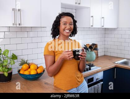 Una giovane donna multietnica si rilassa in una cucina pulita con tazza di caffè Foto Stock