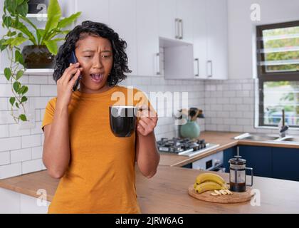 Una giovane donna è sorpresa e scioccata mentre su chiamata in cucina Foto Stock