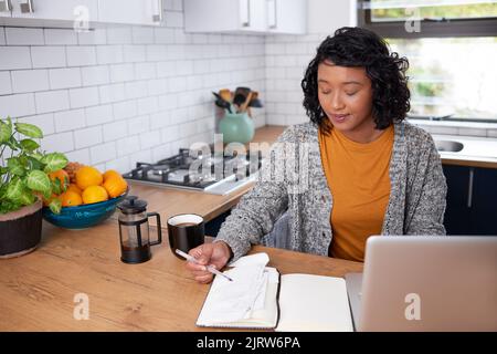 Una giovane donna multietnica rivede le sue finanze familiari in cucina Foto Stock