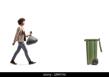 Immagine a profilo intero di un giovane alto che cammina verso un bidone e che trasporta una borsa di plastica isolata su sfondo bianco Foto Stock