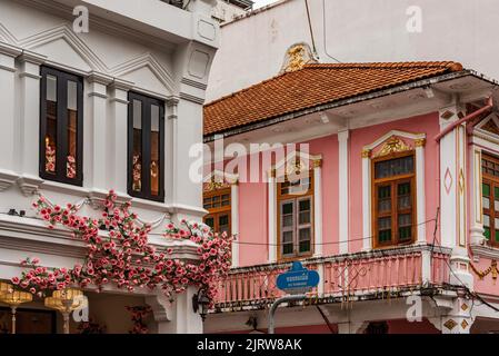 Phuket, Thailandia - 2022 luglio: Edificio bianco con fiori rosa sulla Thalang Road nella città vecchia di Phuket. Alex faccia graffiti murali. Foto Stock