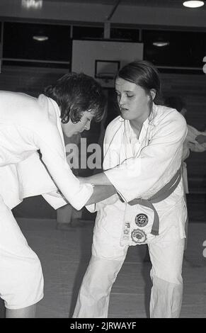 1970s, due giovani donne judo concorrenti in combattimento, con le mani e le braccia bloccate in una posizione di presa in questa arte marziale, Inghilterra, Regno Unito. Badge su una delle giacche, British JUDO Association e Downs. Creato nel 1882 dal Dr. Jigoro Kano, un educatore giapponese come derivazione di un'arte marziale, JUDO non usa armi di percussione o di addestramento come altre arti marziali, con l'accento sul grapping, con il lancio e il lavoro di base. Introdotta nel Regno Unito nel 1918, la British Judo Association è stata fondata nel 1948. Foto Stock