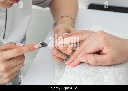 latina manicurista, eseguendo una corretta archiviazione delle unghie per dare loro forma e correggere i bordi irregolari. ragazza esecuzione pratica di archiviazione per ma Foto Stock