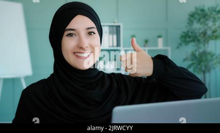 Arabo islamico musulmano studente in hijab nero riuscito businesswoman seduto al posto di lavoro home Office guardando il computer portatile schermo legge bene Foto Stock