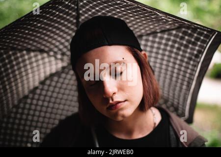 Giovane donna con sopracciglia trafitto che tiene l'ombrello durante la pioggia all'aperto Foto Stock