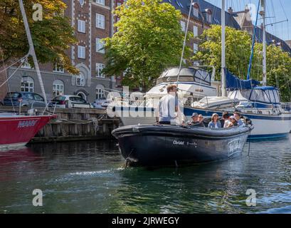 I turisti si godono un piccolo tour guidato in barca di Copenhagen, Danimarca, su una barca che naviga lungo uno dei canali della città sotto il sole luminoso Foto Stock