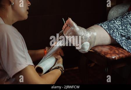 Pedicurist avvolge il piede di un cliente in un involucro di plastica Foto Stock