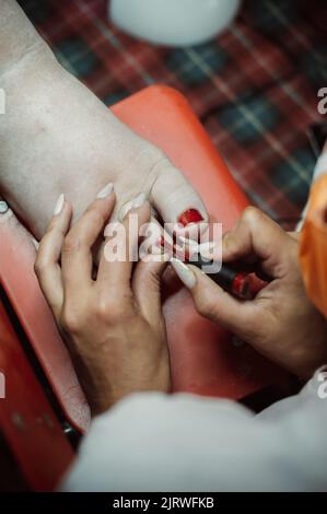 Le mani del pedicurista dipingono le unghie sul piede del cliente con vernice Foto Stock