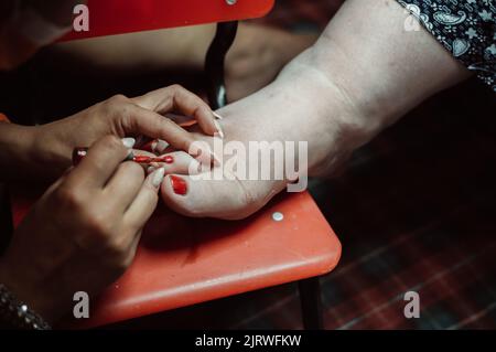 Le mani del pedicurista dipingono le unghie sul piede del cliente con vernice Foto Stock