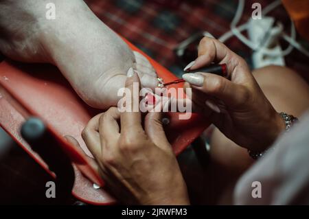 Le mani del pedicurista dipingono le unghie sul piede del cliente con vernice Foto Stock