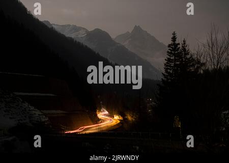 Le auto guidano fino a una strada di montagna ventosa di notte, con una lunga esposizione che mostra una leggera traccia di fari Foto Stock