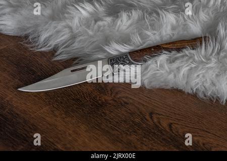 coltello pieghevole e affilato con manico in legno marrone sulla foto di stock di pelliccia di pecora bianca Foto Stock